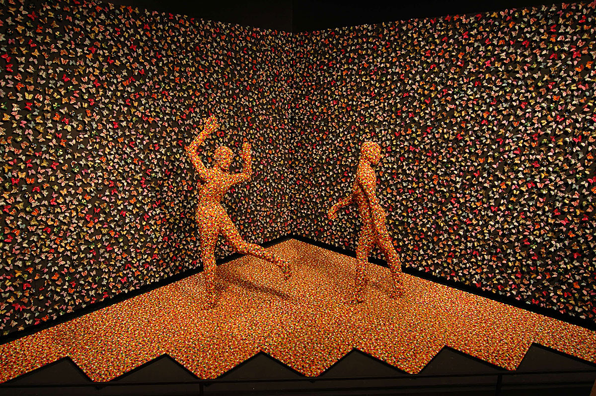 This image shows the installation Shimmering Madness, by Sandy Skoglund, which features two dancing figures covered in jelly beans, as well as hundreds of butterflies.