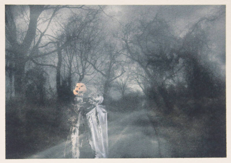 A ghostly black and white image of bare trees along. road with a ghostly superimposed image of a ghost and jack 'o' lantern.